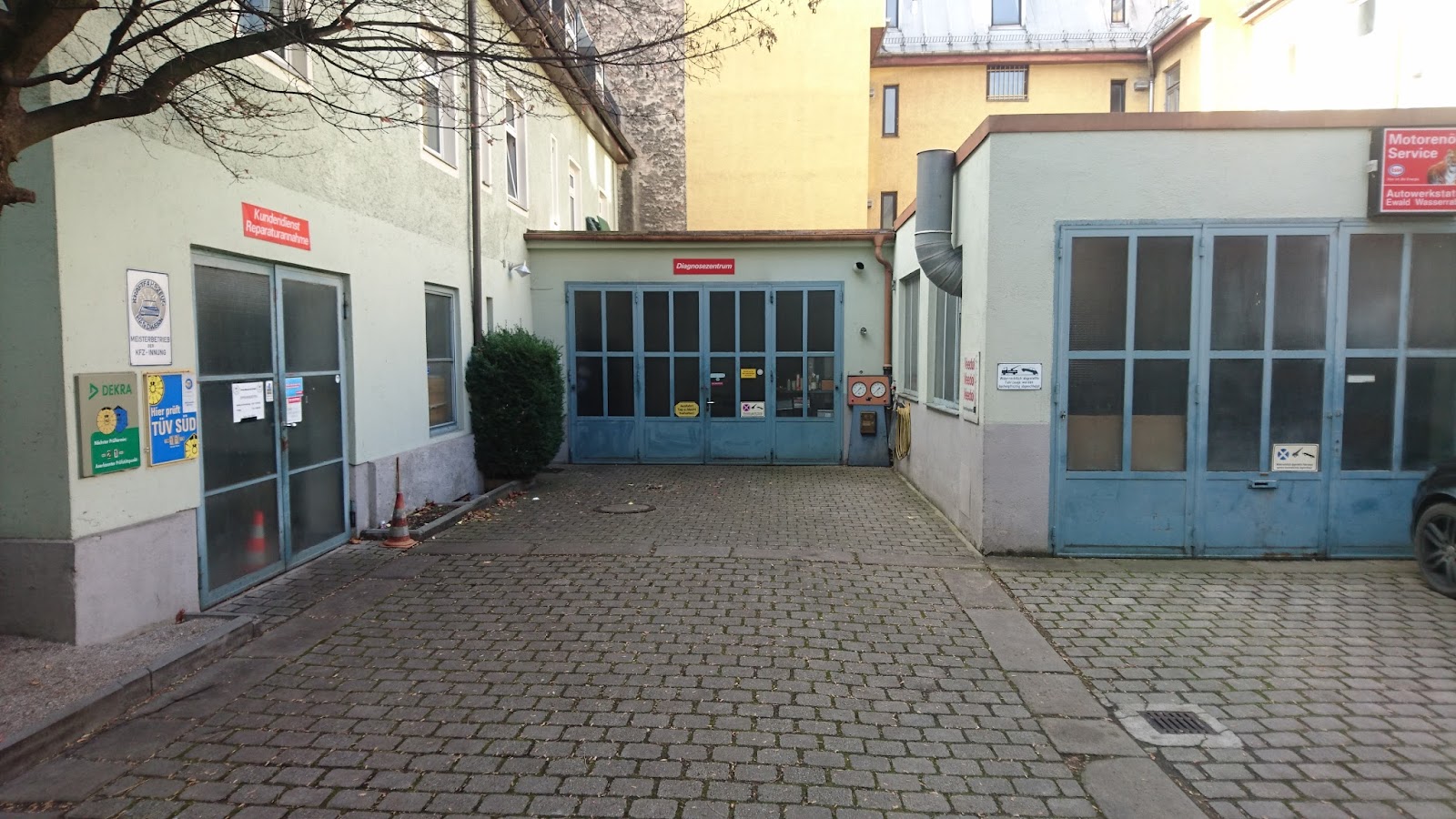 Hof der Wasserrab Autowerkstatt mit den blauen Werkstatttoren, Schildern für Reparaturannahme, Diagnosezentrum, TÜV SÜD und DEKRA